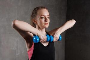 A woman exercises with blue dumbbells in a fitness studio. She performs a strength exercise photo