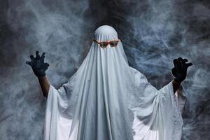 man in scary ghost costume in smoke on grey mysterious background in studio. Minimal halloween ghost concept. photo