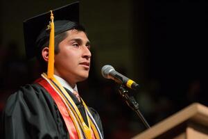 A young man in a graduation gown speaking into a microphone photo