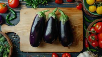 Three eggplants are sitting on a cutting board with other vegetables photo