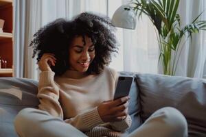 A woman with afro hair sitting on a couch and using her phone photo