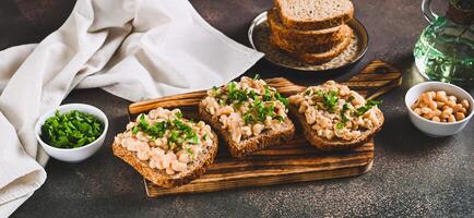 Appetizing sandwiches on grain bread with mashed beans and greens on a board on a table web banner photo
