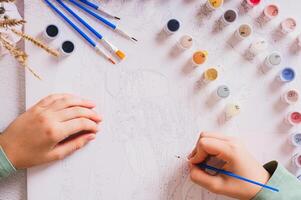 A girl paints a picture by numbers with a brush using a paint set top view photo
