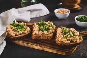 Appetizing sandwiches on grain bread with mashed beans and greens on a board on a table photo