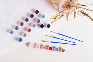 Brushes, multi-colored acrylic paints and canvas for painting by numbers top view photo