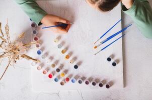 A girl thoughtfully paints a picture by numbers on a table with a brush top view photo