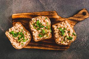 Close up of sandwiches on grain bread with mashed beans and greens on a board top view photo