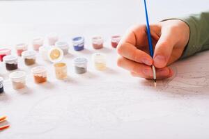 A girl paints a picture by numbers with a brush using a paint set on the table photo