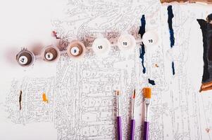 Several containers of paints and brushes on a painting by numbers top view photo