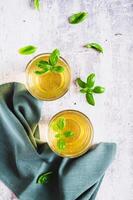 Refreshing summer basil lemonade with leaves in glasses on table top and vertical view photo