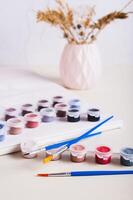 Brushes, multi-colored acrylic paints and canvas for painting by numbers vertical view photo