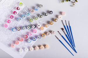 Painting by numbers kit, paints, brushes and paper on table top view photo