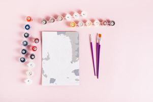 Paint by numbers kit and started painting on pink background top view photo