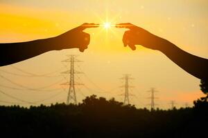 Hands Touching Under Bright Light, Energy Transfer Concept with Power Lines at Sunset in Background photo