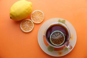 Enjoy a Delightful Fresh Lemon Tea with Invigorating Citrus Slices on a Vibrant Orange Background photo