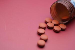 A Collection of Scattered Tablets from a Medicine Bottle Spread across a Soft Pink Background photo