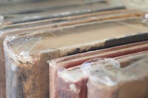 A collection of vintage books, neatly stacked on a shelf, protected in plastic coverings photo