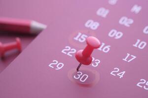 A closeup of a vibrant pink calendar with a colorful pushpin for effective event planning photo
