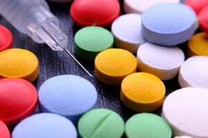 A Colorful Assortment of Various Pills and a Syringe Displayed on a Dark Background photo