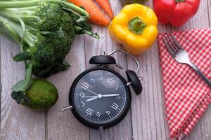 A beautiful arrangement of Fresh Vegetables with an Alarm Clock placed on a Rustic Wooden Background photo