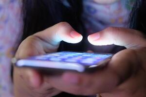 This is a closeup image featuring hands actively using a smartphone in low, dim lighting photo