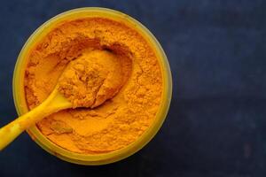 A captivating display of vibrant turmeric powder in a container, with a spoon for cooking photo