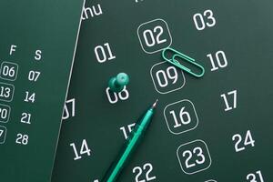 A calendar with a pen and paperclip on a dark surface creates an intriguing aesthetic photo