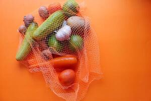 A variety of Fresh Vegetables presented in a Net Bag against a Vibrant Orange Background photo