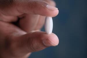 A detailed closeup view of a human hand comfortably gripping a small white pill tightly photo