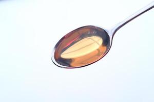 Closeup of a shiny spoon with golden honey on it, resting on a reflective surface photo