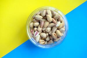 Savor the delicious pistachio nuts in a clear container on a colorful background, enticing you photo
