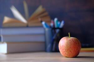 A vibrant apple placed on a desk surrounded by books and various stationery items in the background photo