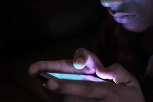 This image captures a closeup view of hands engaged with a smartphone amidst complete darkness photo