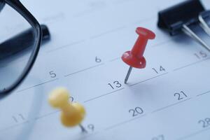 Brightly colored push pins affixed on a calendar, accompanied by a pair of reading glasses photo