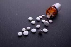 Numerous Scattered White Pills from an Open Prescription Bottle on a Black Surface photo
