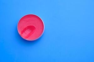 A vibrant pink cream beautifully displayed in a round container resting on a bright blue background photo