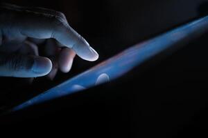 A closeup image showcases a hand actively interacting with a glowing tablet screen in the dim light photo