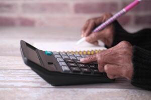 A Person is Actively Utilizing a Calculator While Also Taking Notes with a Pink Colored Pen photo