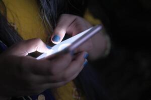 A person is using a glowing smartphone while immersed in a dimly lit environment around them photo