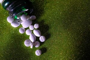 A mess of scattered pills along with a medicine bottle displayed prominently on a green background photo