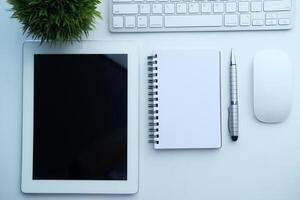 A beautifully minimalistic workspace setup featuring a tablet, notebook, and a plant photo