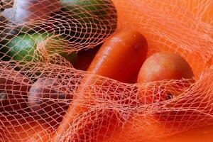 A Variety of Colorful Vegetables Encased in Bright Orange Mesh Netting for Display photo