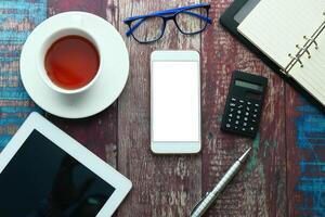 A wellarranged work desk setup featuring a mobile phone, a tablet, a calculator, and a cup of tea photo