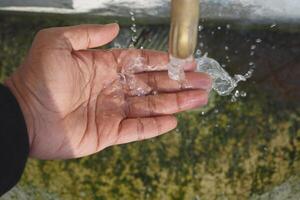 A Person Actively Catching Fresh Water Flowing from a Faucet, Emphasizing Cleanliness and Freshness photo