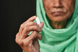 An Elderly Woman Carefully Holding a Pill with Great Care and Attention to Detail photo