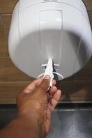 A hand is utilizing a paper towel dispenser located in a restroom for convenience and hygiene photo