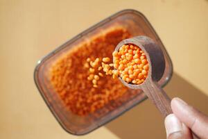 A hand holds a measuring spoon of red lentils above a container ready to be filled photo
