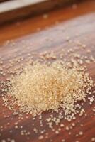 This image features a closeup view of a pile of brown sugar resting on a wooden surface photo