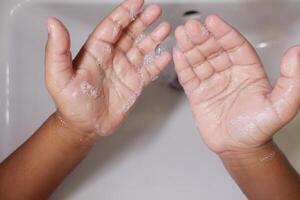 child making a cleansing gesture with soap and water on hands photo