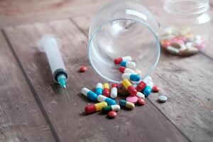 A vibrant array of colorful pills and a syringe situated on an aged wooden surface photo
